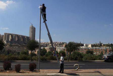 An Ultra Orthodox Jewish man stands on a  ladder and hangs "Eruv" (Eiruv or Erub) wire, near the Gilo neighborhood in south Jerusalem, on Friday, Aug 14, 2009. A community Eruv refers to the legal aggregation or "mixture" under Jewish religious property law of separate parcels of property meeting certain requirements into a single parcel held in common by all the holders of the original parcels, which enables Jews who observe the traditional rules concerning Shabbat to carry children and belongings anywhere within the jointly held property without transgressing the prohibition against carrying a burden across a property line on the Jewish sabbath. Photo by Nati Shohat / FLASH90. *** Local Caption *** ÚÈ¯Â· ÁÂË ÚÓÂ„ Á¯„ÈÌ Á¯„È È¯Â˘ÏÈÌ